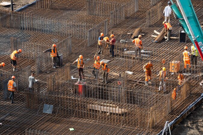 concreting work: construction site worker during concrete pouring into formwork at building area with skip.