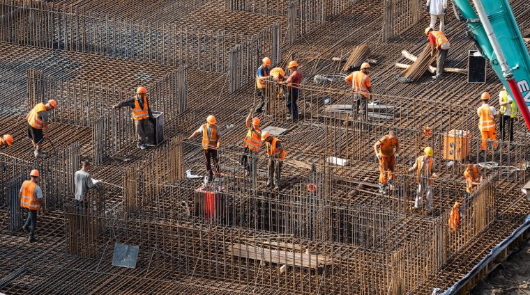 concreting work: construction site worker during concrete pouring into formwork at building area with skip.